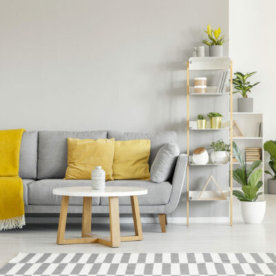 Yellow pillows and blanket on grey sofa in modern living room interior with plants and carpet. Real photo