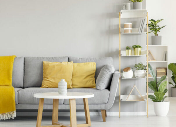 Yellow pillows and blanket on grey sofa in modern living room interior with plants and carpet. Real photo